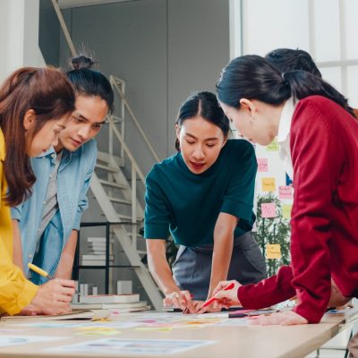 Asian businessmen and businesswomen meeting brainstorming ideas about creative web design planning application and developing template layout for mobile phone project working together in small office.